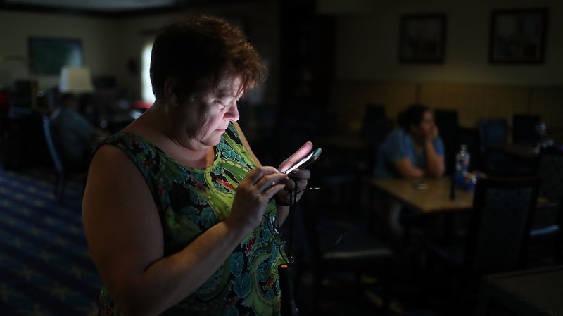 Amy Currin watches the weather news on her cell phone after the power went out at the hotel where she was taking shelter from Hurricane Harvey last August.