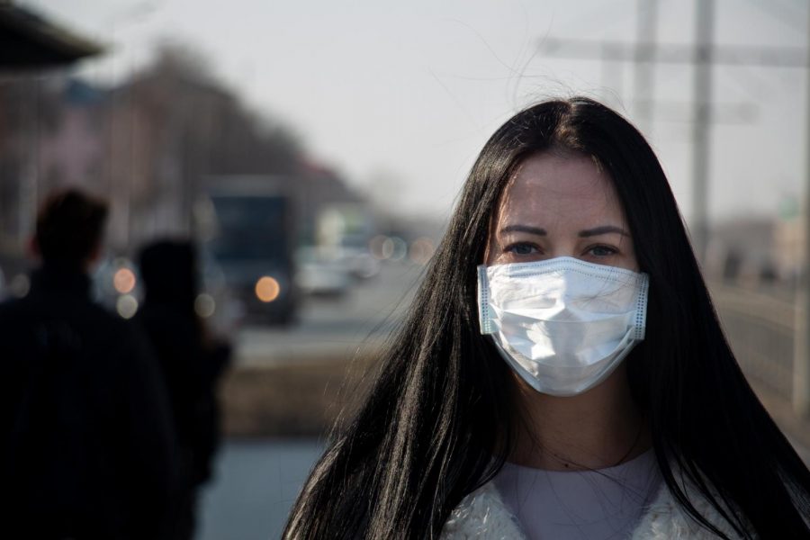 A young woman standing in front of a road, wearing a mask, which is one of the factors to avoiding the coronavirus.