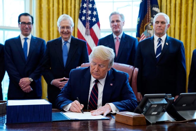 President Trump signs stimulus relief package with men smiling behind him.