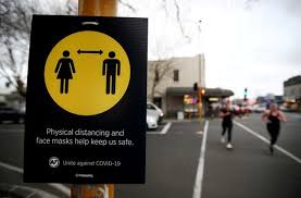 People jog past a social distancing sign on the first day of New Zealand's new COVID-19 safety measure that mandates wearing of a mask on public transport, in Auckland, New Zealand, August 31, 2020.