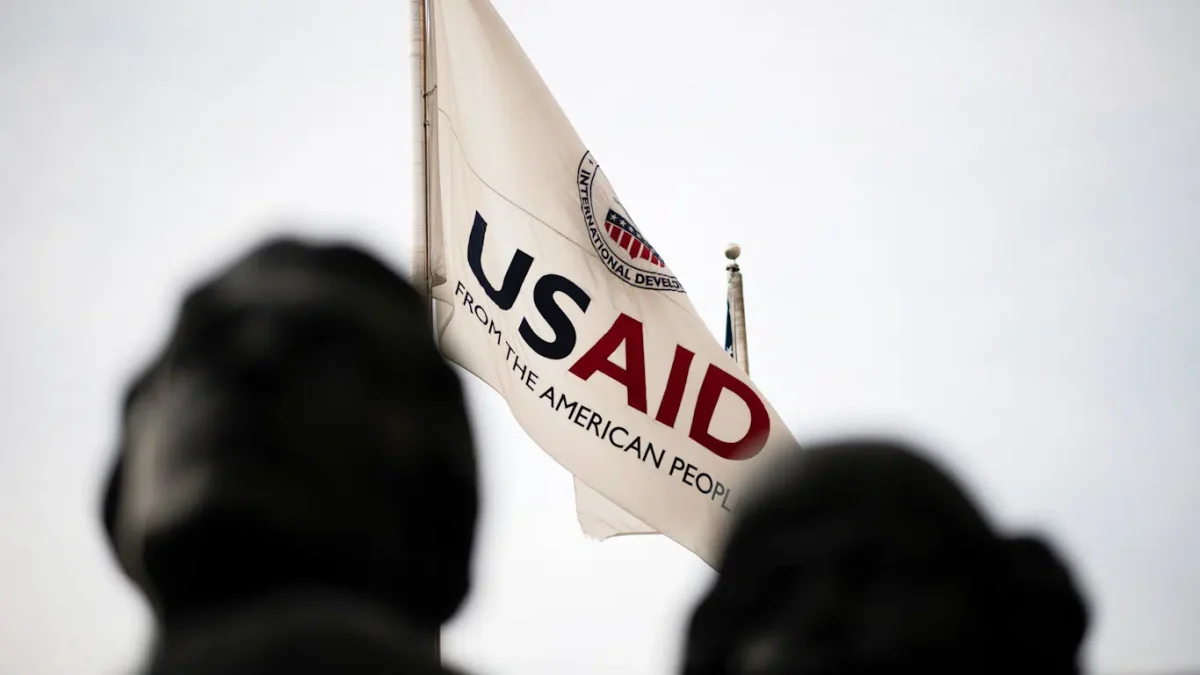 USAID flag flies in background over heads of statues. 